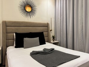 A hotel room with a bed, a headboard, a wall-mounted light fixture, a nightstand, and a window with curtains. - Luxury 4-Bedroom Villa with Private Pool & Beach Access (Punta Cana)