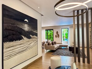 Ein modernes Wohnzimmer mit einem großen abstrakten Gemälde, einer runden Leuchte und Blick auf Grün durch große Fenster.