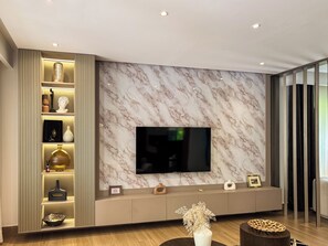 A modern living room with a marble wall, a flat-screen TV, and a built-in shelving unit with decorative items. - Luxury 4-Bedroom Villa with Private Pool & Beach Access (Punta Cana)