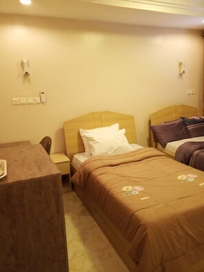 Ein Hotelzimmer mit einem Einzelbett, einem Nachttisch aus Holz, einem Schreibtisch und einem Stuhl.