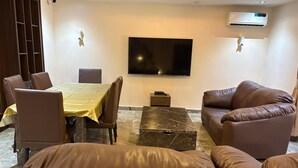 A living room with a dining table, leather sofas, a flat-screen TV, and an air conditioning unit. - Luxury stylish premium Home in Prime Location, Exceptional Hospitality (Abuja)