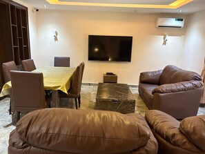 Ein Wohnzimmer mit Esstisch, Ledersofas, einem Flachbildfernseher und einer Klimaanlage.
