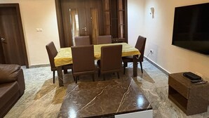 A dining area with a marble floor, a table with chairs, a sofa, a TV, and a small wooden side table. - Luxury stylish premium Home in Prime Location, Exceptional Hospitality (Abuja)
