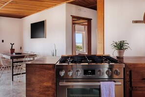 A modern kitchen with a Bosch gas stove, oven, and a dining area with a table and chairs. - Adobe + Casita | Sleeps 6 | 10 Min to Big Bend (Terlingua)