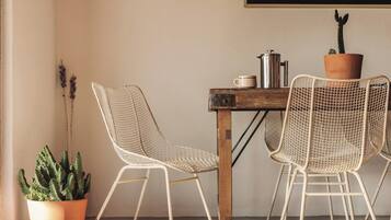 Une pièce comprenant une table et deux chaises en treillis métallique, un cactus en pot et une cafetière en métal.