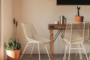 Et værelse med et bord, to stole med metalnet, en potte med kaktus og en metal kaffekande.
