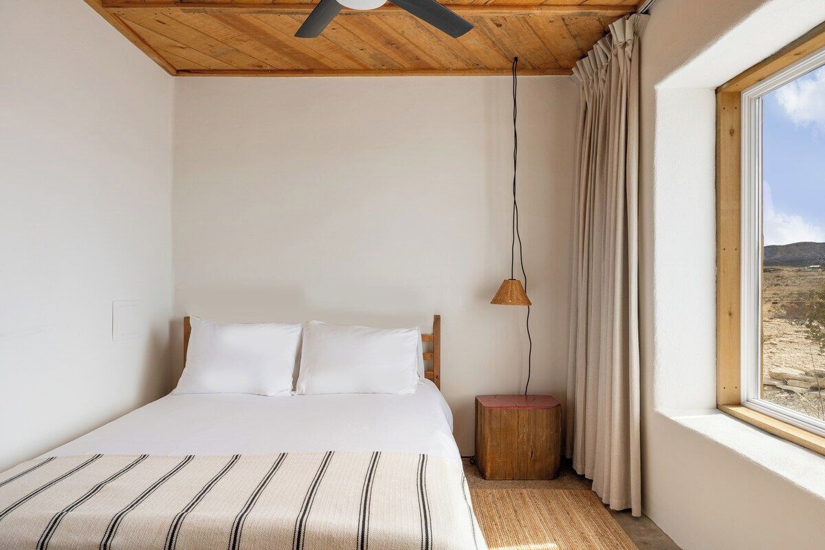 Une chambre à coucher avec un lit, un plafond en bois, une fenêtre avec des rideaux et une lampe sur une table de chevet.