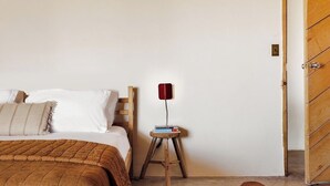 Een slaapkamer met een bed, een houten nachtkastje met boeken, een rode lamp en een houten deur.