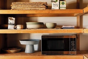 A kitchen with a microwave, stacked plates, bowls, and a coffee bag on the shelves. - Adobe + Casita | Sleeps 6 | 10 Min to Big Bend (Terlingua)