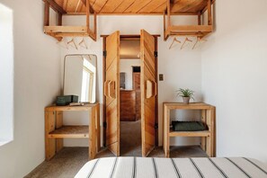 Une pièce comprenant un lit, des meubles en bois, un miroir et une porte donnant sur une autre pièce.