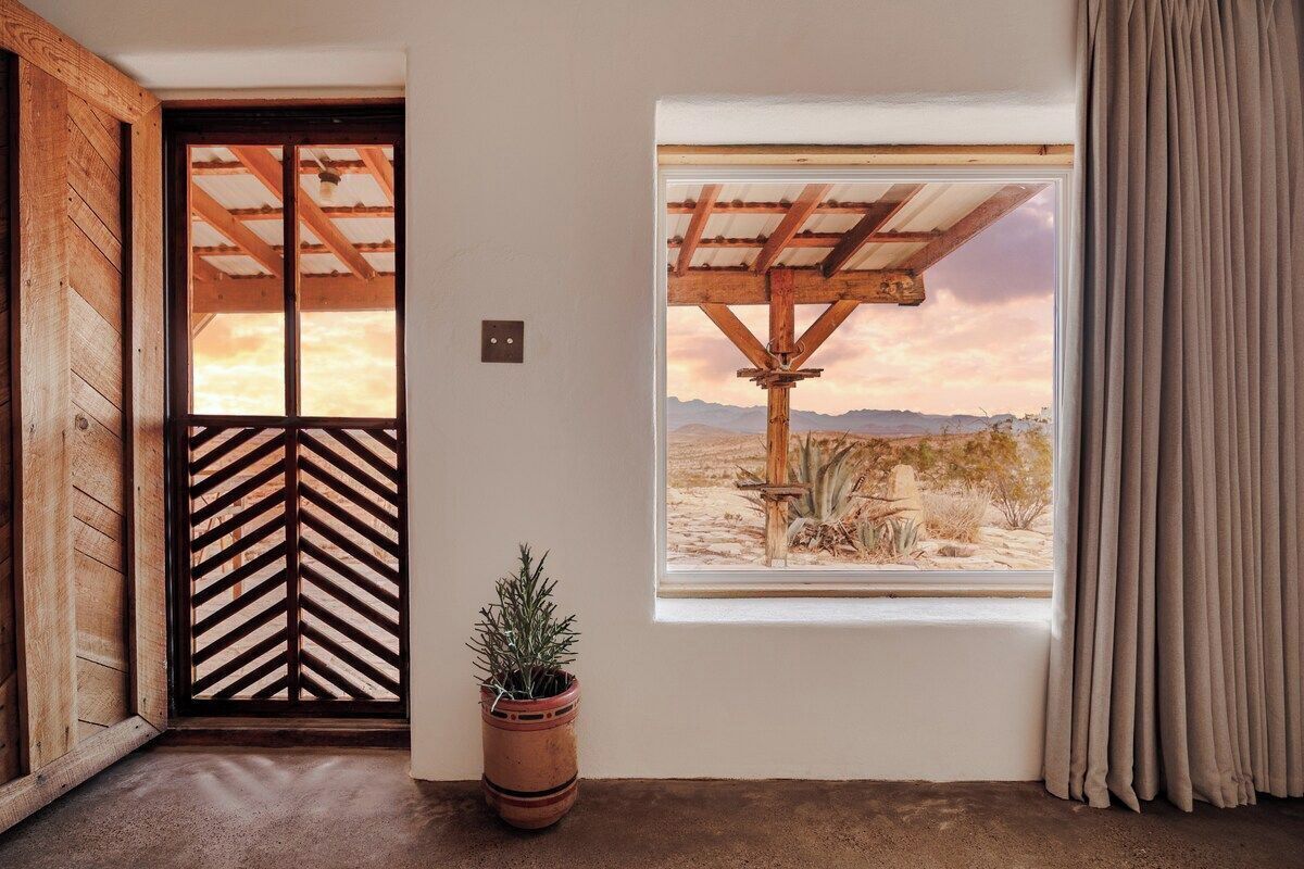 A room with a wooden door, a window with a view of a desert landscape, and a potted plant.