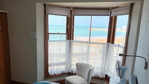 Un dormitorio con cama, una silla, una mesita de noche, una lámpara y vista al mar.