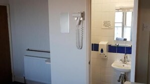 Habitación de hotel con cama, baño con inodoro, lavamanos y secador de pelo en la pared.