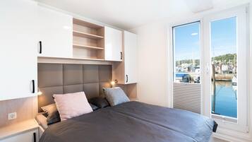 Una camera da letto con un letto grande, armadi a muro e vista su un porto turistico attraverso un'ampia finestra.