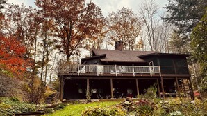 A rustic cabin with a wooden deck and a stone wall in front. - Quintessential Berkshire Escape - Artist Home, Tucked Away in Nature (Otis)