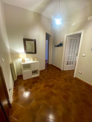 Un couloir avec une coiffeuse blanche, un miroir, un radiateur et une porte dotée d’un panneau en verre dépoli.