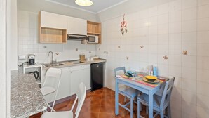 Una cucina compatta con zona pranzo, pareti in piastrelle bianche e una lampada a soffitto.
