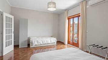 A bedroom with a bed, a bench, a door, and a view of the outside.