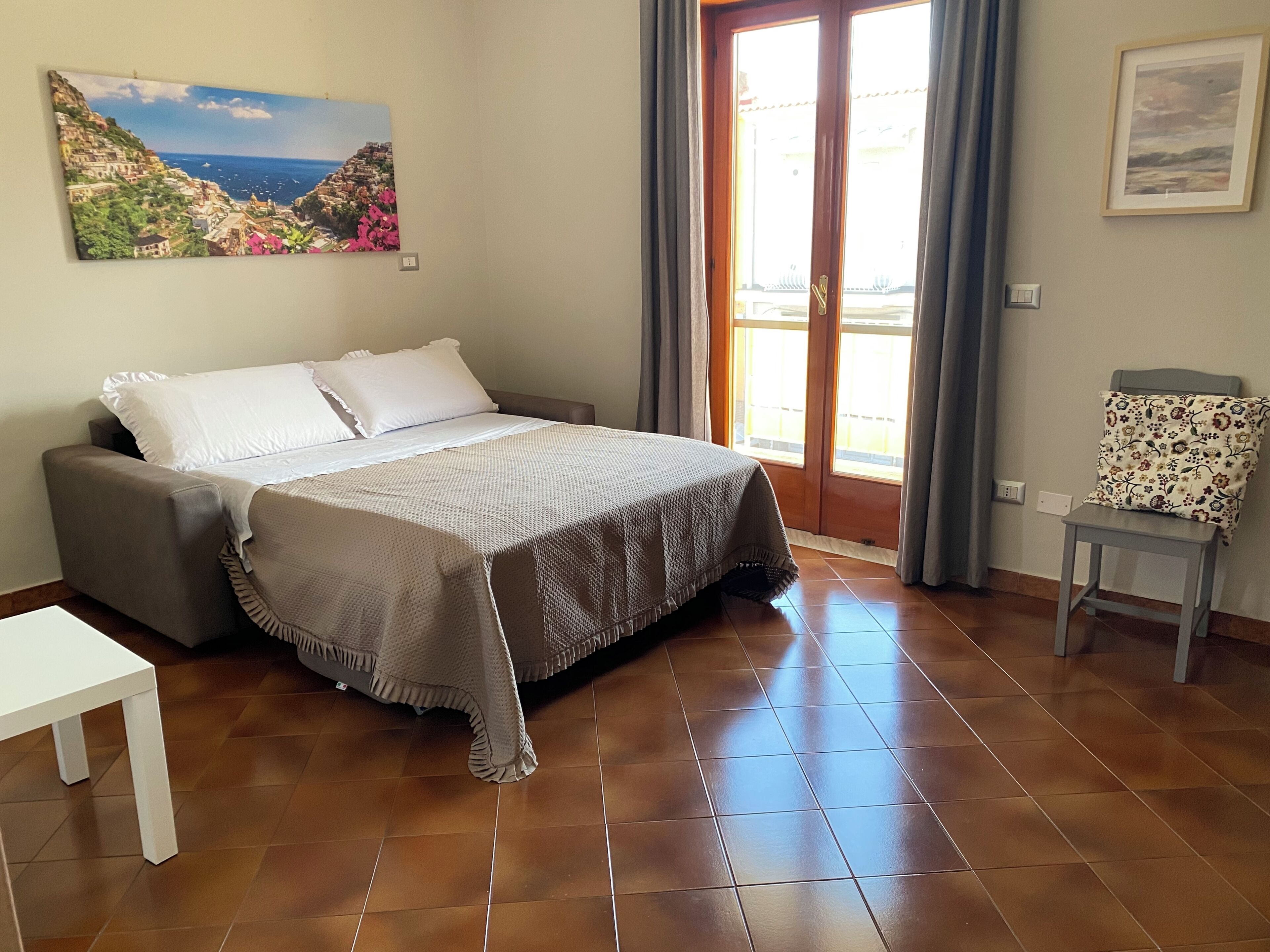 Een slaapkamer met een bed, een bank, een tafeltje en uitzicht op de omgeving via een deur.