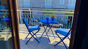 Un balcone con due sedie blu e un tavolino, con vista su una strada con auto parcheggiate e palazzi.