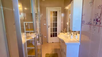 Un baño moderno con cabina de ducha de vidrio, un lavamanos blanco y suelo de baldosas color beige.