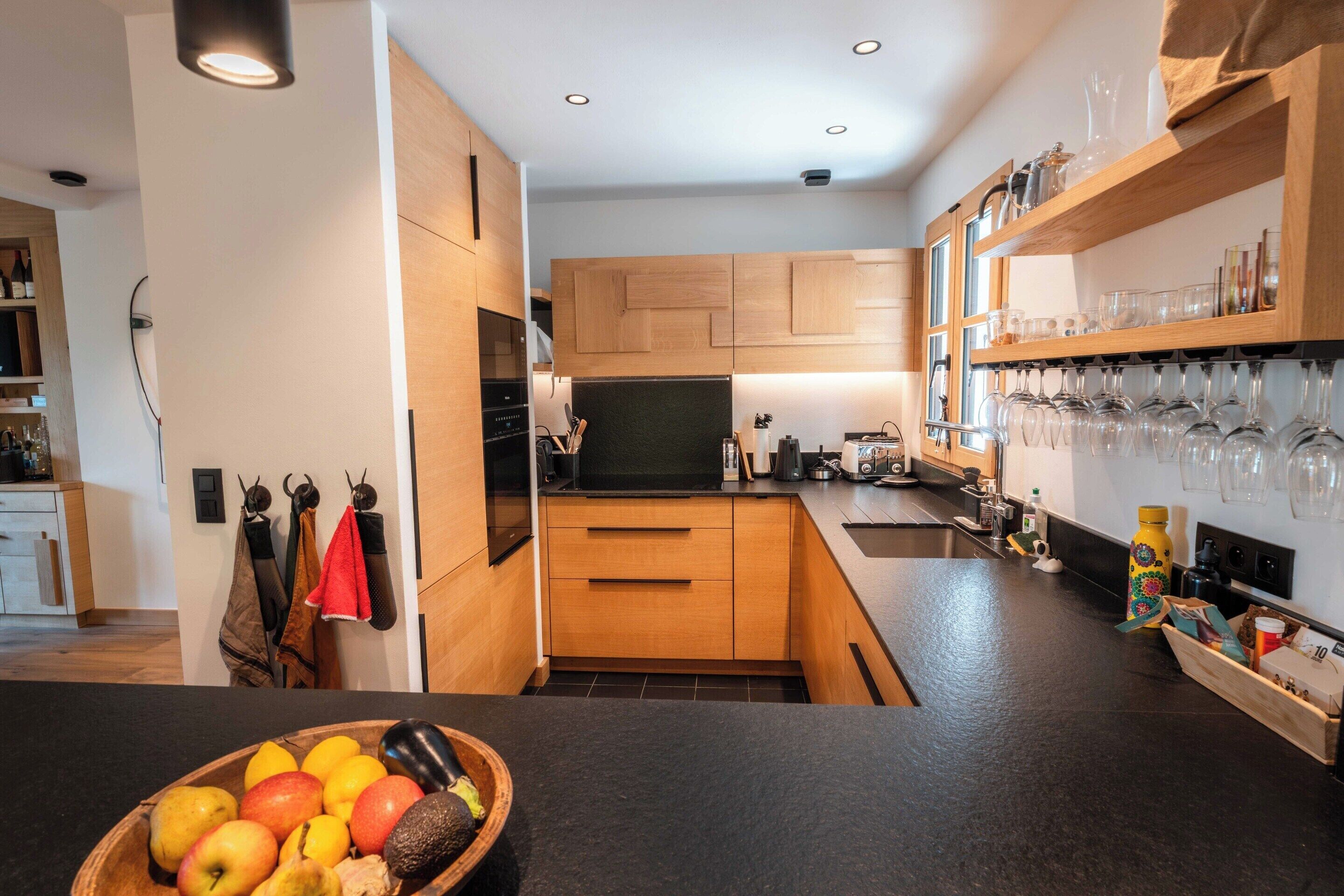 A modern kitchen with wooden cabinets, a black countertop, and a bowl of fruit.