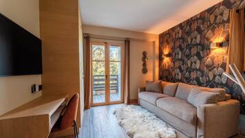 A modern living room with a sofa, a flat-screen TV, a wooden desk, and a large window with a view of trees.