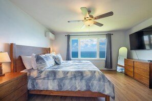 Ein Schlafzimmer mit einem Bett, einem Deckenventilator, einem Fenster mit Meerblick, einem Fernseher und einer Kommode.
