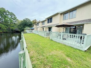 Une propriété située au bord de l’eau, dotée d’une terrasse enherbée, d’une clôture en bois et d’un bâtiment avec un patio couvert.