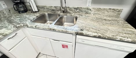 A kitchen with a double sink, a coffee maker, and a dishwasher.