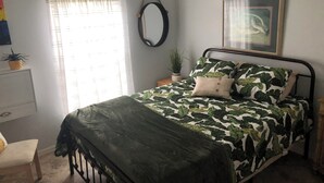 A bedroom with a bed, a bedside table, a mirror, and a window with curtains.