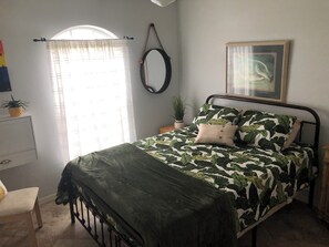 A bedroom with a bed, a bedside table, a mirror, and a window with curtains.