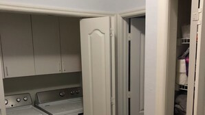 A laundry room with two front-loading washing machines and a dryer, a white door, and a closet with shelves.