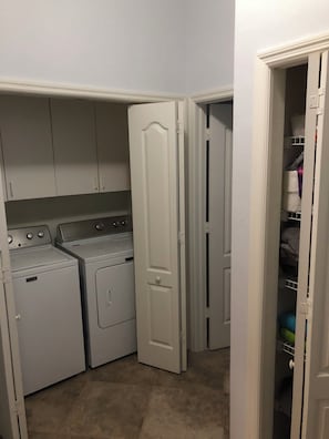 A laundry room with two front-loading washing machines and a dryer, a white door, and a closet with shelves.