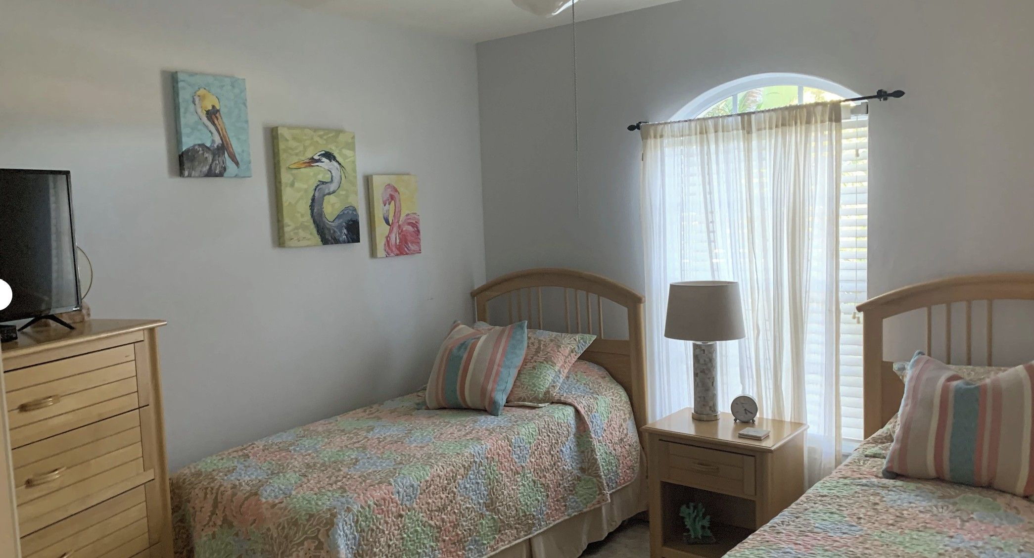 A bedroom with two single beds, a nightstand with a lamp, a dresser, and wall art.