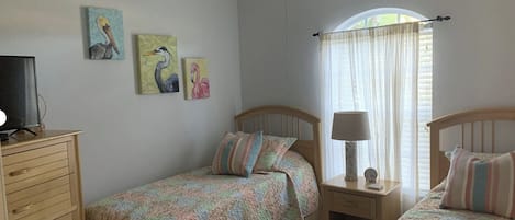 A bedroom with two single beds, a nightstand with a lamp, a dresser, and wall art.
