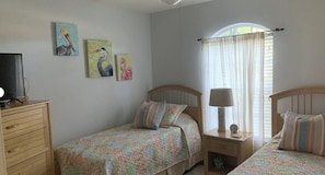 A bedroom with two single beds, a nightstand with a lamp, a dresser, and wall art.