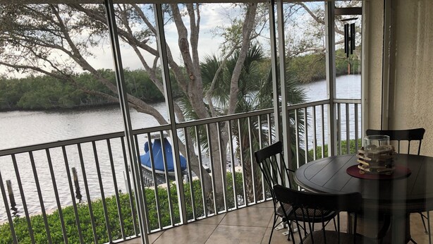 A balcony with a view of a river, a dining table with chairs, and a glass sculpture.