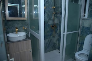 Un baño con un lavabo blanco, un espejo, cabina de ducha y un inodoro.