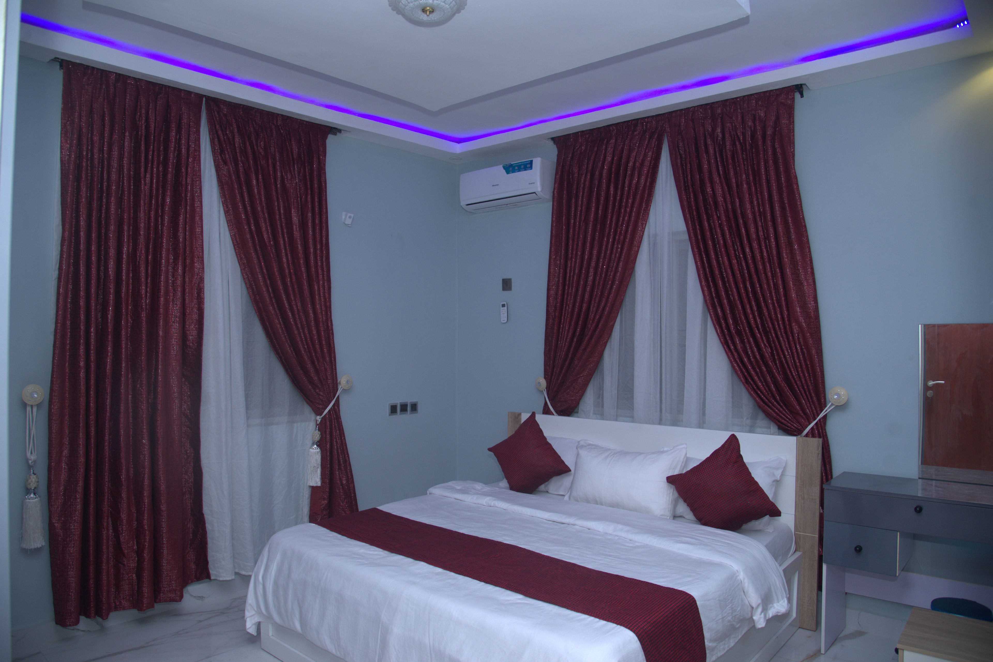A bedroom with a bed, curtains, an air conditioning unit, and a nightstand.