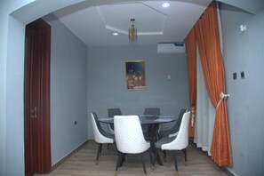 Un comedor con una mesa y sillas de vidrio, una lámpara en el techo y un equipo de aire acondicionado.