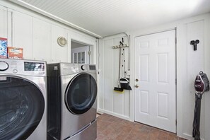 A laundry room with two front-loading washing machines, a door with a coat rack, and a parking meter. - Be A Nomad | 3BR With Pool (Jacksonville Beach)