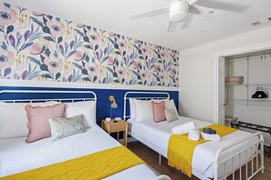 A hotel room with two beds, a ceiling fan, a wall with floral wallpaper, and a wardrobe. - Be A Nomad | 3BR With Pool (Jacksonville Beach)