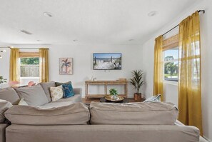 A living room with a sofa, a coffee table, and a painting on the wall. - Be A Nomad | 3BR With Pool (Jacksonville Beach)