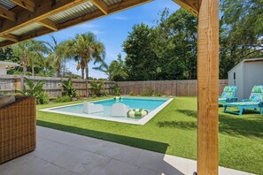 A backyard with a swimming pool, a covered patio, and a wooden fence. - Be A Nomad | 3BR With Pool (Jacksonville Beach)