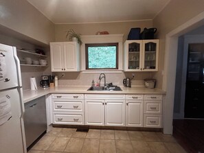 A kitchen with white cabinets, a sink, and a window with a view of greenery. - Bright Heritage Home | 2BR | Central | Foodie Hub (Calgary)