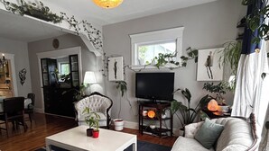 Uma sala de estar com televisão, sofá, poltrona, mesa de centro e diversas plantas.