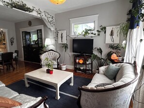 A living room with a television, a sofa, a chair, a coffee table, and various plants. - Bright Heritage Home | 2BR | Central | Foodie Hub (Calgary)