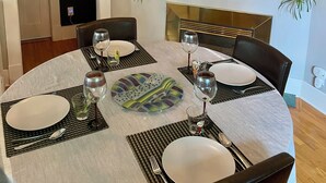 Uma sala de jantar com um lustre, mesa redonda, cadeiras e um relógio na parede.