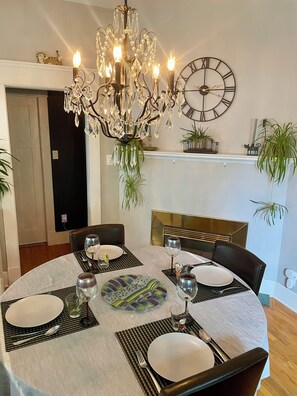 A dining area with a chandelier, round table, chairs, and a clock on the wall. - Bright Heritage Home | 2BR | Central | Foodie Hub (Calgary)